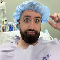 Chet, who received a cochlear implant after losing his hearing from a rare autoimmune disease, in a selfie just before surgery wearing a hospital gown and hair cap. 