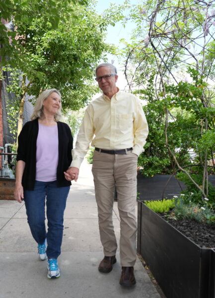 A photo of loves ones, a mature adult man and his wife, walking hand-in-hand through a garden smiling at each other. 