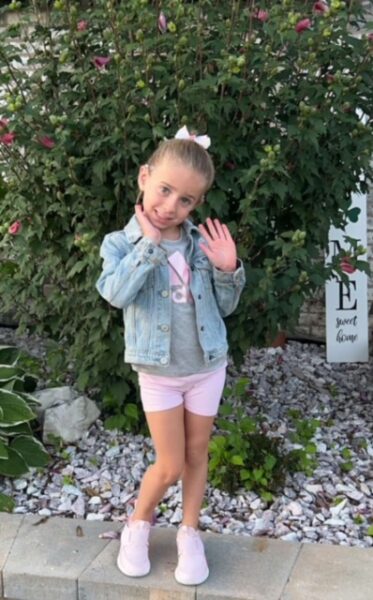 Abby, a young cochlear implant recipient posing for a photo and holding her hands up in the air. 