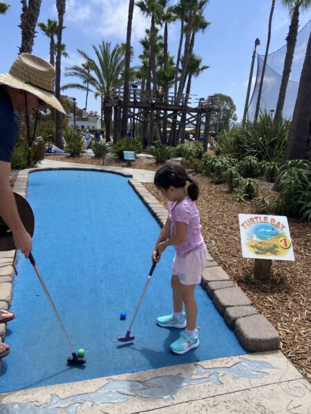 Adrian, a child who uses the Osia System, playing putt putt golf in what looks like a tropical setting.