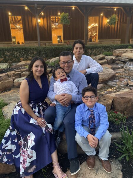 A family photo of Helio, his mother, father and two brothers Alonso and Marcel. They are all dressed in formal attire and smiling, while sitting on a rock feature. 