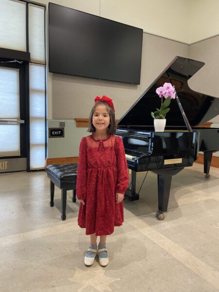 Adrian, a child who uses the Osia System, smiling in front of a grand piano.