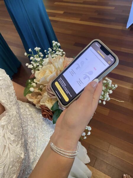 A picture of Kristina holding her phone out above her bouquet on her wedding day, and adjusting the Nucleus Smart App settings on her cell phone. 