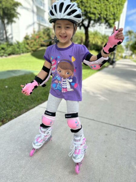 Arielle, who along with her sibling, has hearing loss from MYO15A, shown smiling as she rollerblades on a sidewalk on a sunny day.