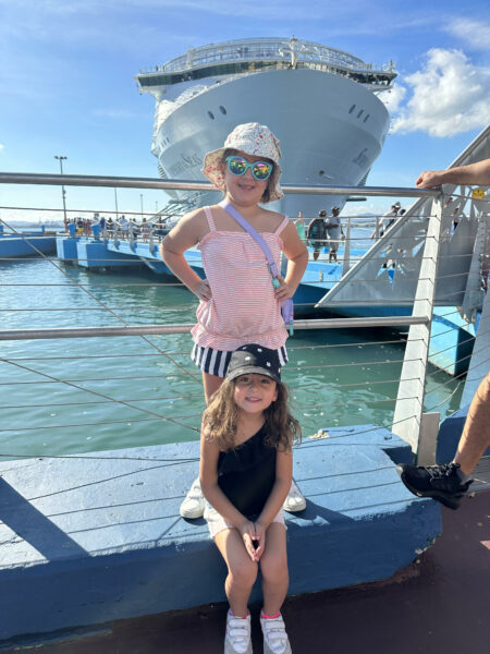 Siblings, who have hearing loss from MYO15A, smiling for a photo, while sitting on a pier in front of a cruise ship.