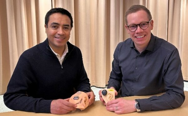 Ivan Gonzalez (left) and Daniel Rhodin (right) – Alt. Text: two men, Ivan and Daniel, pictured sitting at a table and holding ear models with the Osia System attached. 