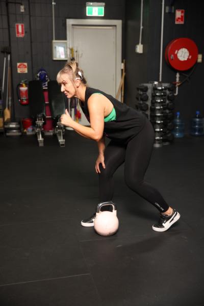 A woman being active with her cochlear implant, in the gym with a kettlebell 