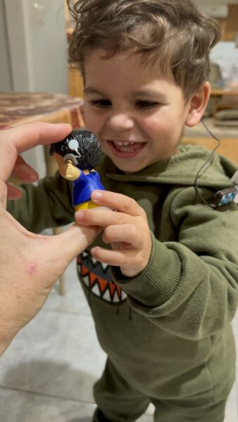 Augustine who has cochlear implants to help with Mitchell Syndrome laughing and smiling while seeing a small figurine also wearing a cochlear implant.