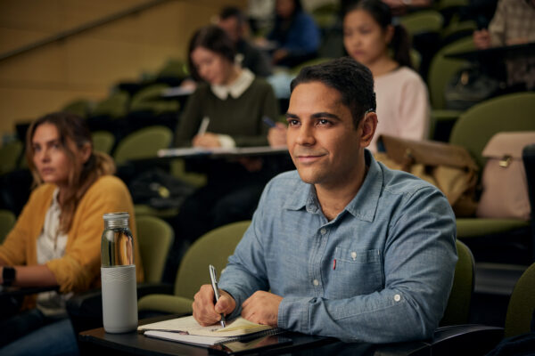 A young man sits in a lecture hall listening intently in his cochlear implant; navigating listening fatigue.