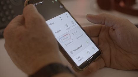  Two hands hold a phone which displays the Cochlear Nucleus Smart App settings.