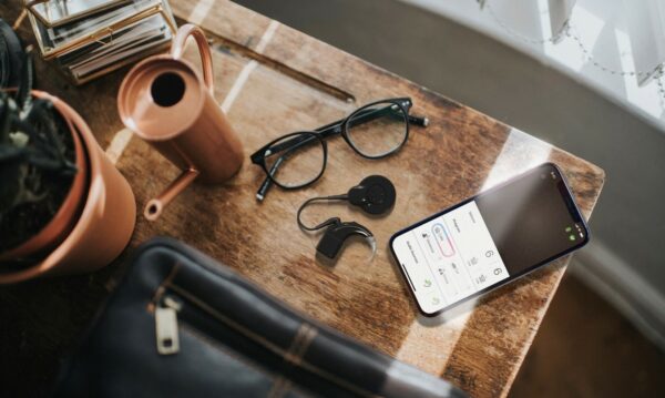 Wooden table showing glasses, a plant, a phone abd other items. Hearing with a Cochlear Nucleus 8 Nexa Sound Processor and other items.