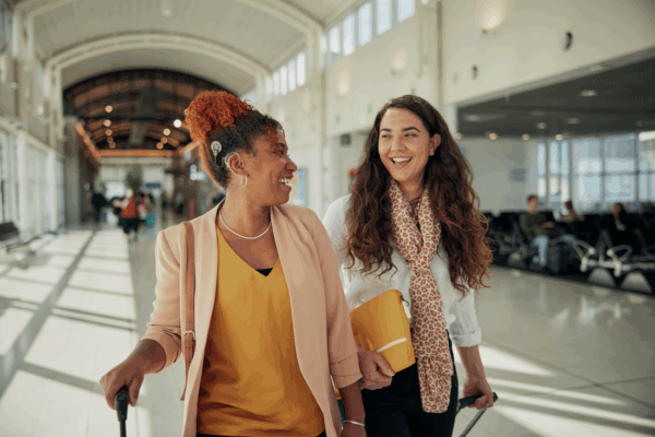 Two women walking in the airport, one of whom is wearing a Cochlear Nucleus 8 Sound Processor; travel checklist with a cochlear implant.