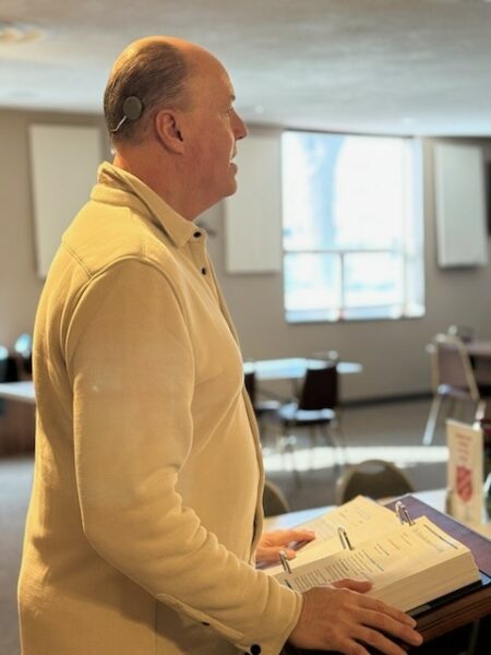 Jeff, standing in church speaking to the church congregation, showing his Osia 2 Sound Processor; Osia System hearing details