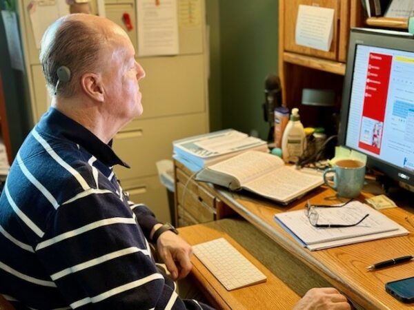 Jeff, sitting at his desk looking at his computer screen, showing his Osia 2 Sound Processor; Osia System hearing details
