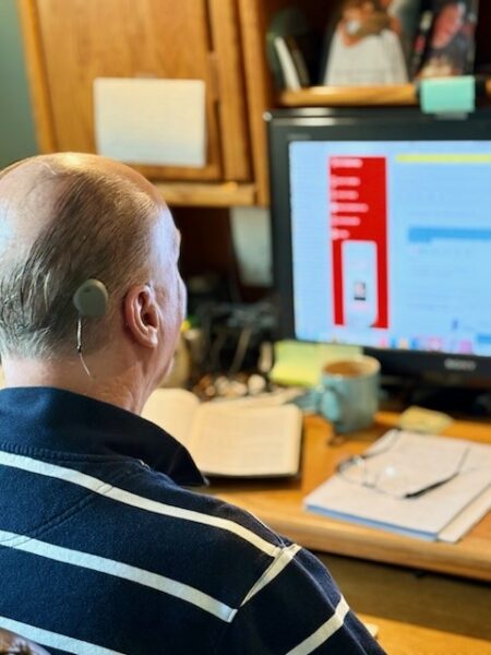 Jeff, sitting at his desk at his computer displaying his Osia 2 Sound Processor; Osia System hearing details