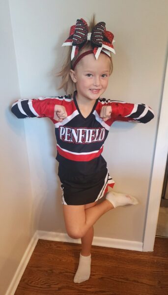 Lyla, a young girl with unilateral hearing loss who received a cochlear implant, wearing a cheerleader uniform and posing in a stance.