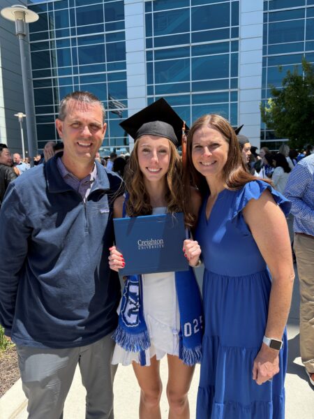 Addy (pictured middle), a girl with single-sided deafness who uses the Osia System, smiling for a photo with her parents after her graduation. She is holding her degree.