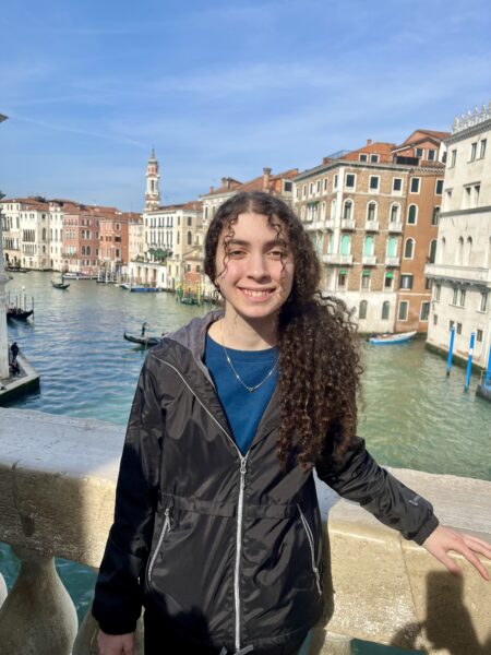 Brynn, a Cochlear™ recipient, pictured smiling in front of a canal in Venice, Italy.