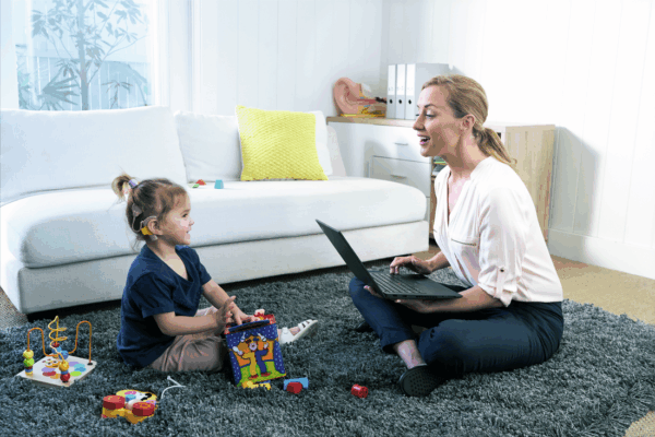 A woman and a young girl with a cochlear implant sit on a carpeted floor playing with toys.