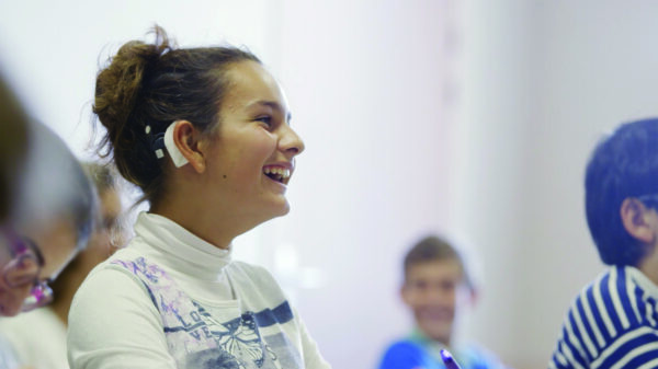 Girl smiling in school with classmates showing her white Nucleus sound processor.