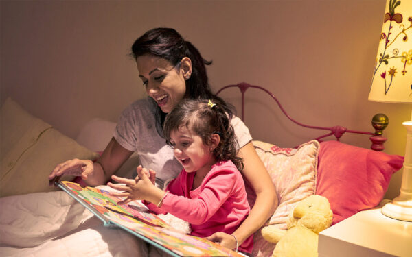 Little girl and woman read a book in bed next to a bedside lamp