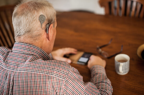 Man wearing a Cochlear Nucleus 8 Sound Processor sits at a table looking at his phone.