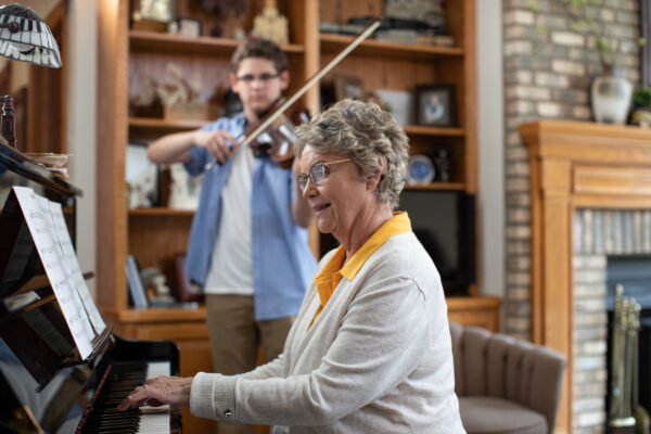 An woman, wearing a Cochlear™ Nucleus® 8 Sound Processor plays the piano while a teen age child plays the violin next to her