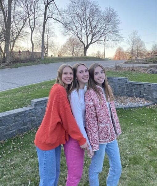 Addy (pictured right), a girl with single-sided deafness who uses the Osia System, standing with her 2 sisters smiling for a picture. 