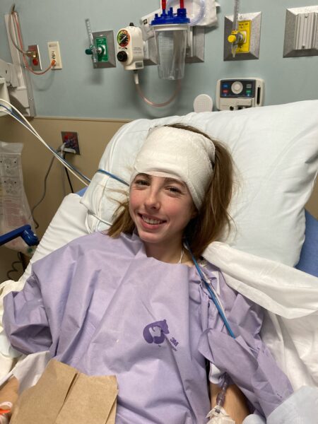Addy, a girl with single-sided deafness who uses the Osia System, smiling in a hospital bed with a headwrap after her surgery.