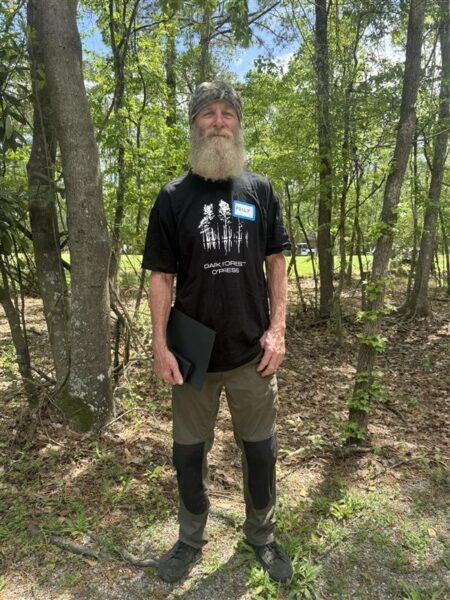 Kelly, a cochlear implant recipient who plays guitar, stands in a forest.