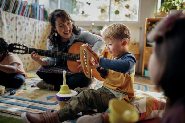 Children and a woman playing musical instruments in a colorful classroom. A little boy wearing a Nucleus 8 Sound Processor sits in the foreground participating with the class.