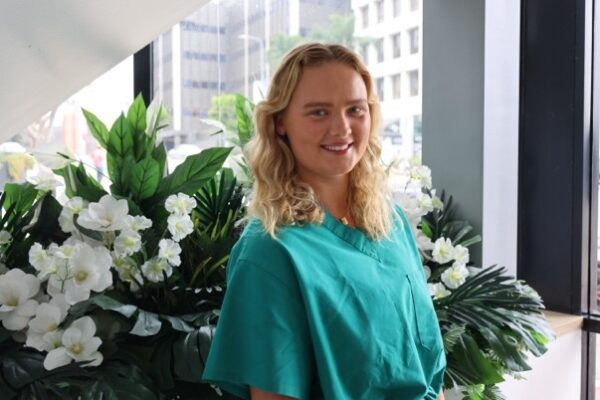 Mathilde, a recipient of cochlear implants, posing for a professional photo in front of a large white floral display, smiling in teal scrubs.