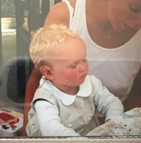 Mathilde, a recipient of cochlear implants, pictured as a very young girl, sitting in her mother's lap, her behind-the-ear cochlear implant device is shown above her ear.