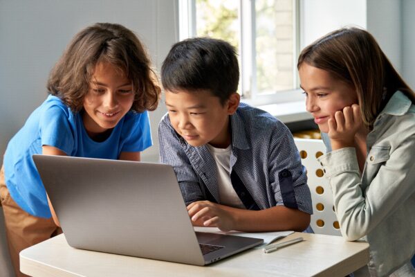 Three children look at a laptop screen together.