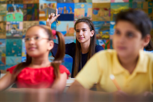 A teen girl raises her hand in class.