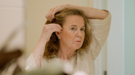 A recipient is facing a mirror, placing a Cochlear Nucleus 8 Sound Processor above her right ear. 