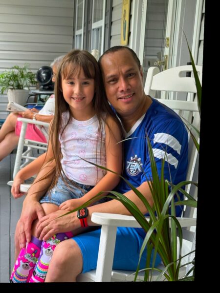 Charles, whose Osia System helped his hearing journey, pictured in a rocking chair on a patio, with his niece sitting on his lap. 