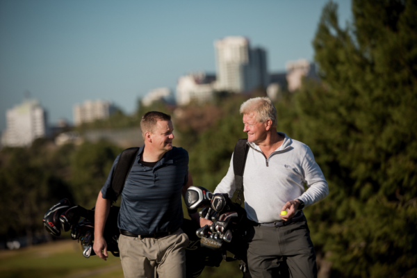  Two men walking with golf bags, talking, with trees and buildings in the background; new sound processor.