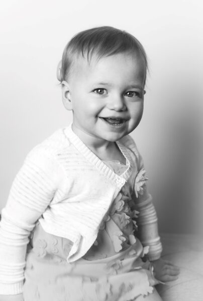 Piper, a young girl with bilateral Kanso 2 Sound Processors, pictured at 17-months-old smiling for a picture in a fluffy dress.