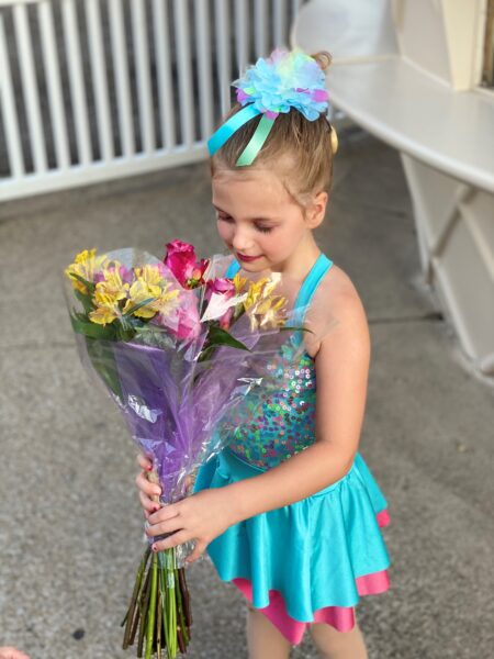 Piper, who has bilateral Kanso 2 Sound Processors, pictured in a blue and pink dress after a dance event, smelling a bouquet of flowers.