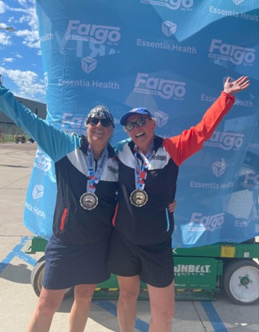 Tracy, who received clarity from her cochlear implant, standing with a friend after the Fargo Half Marathon race, they are both smiling with finisher medals around their necks.