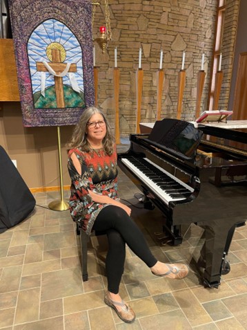 Tracy, who received clarity from her cochlear implant, pictured on a piano bench with a glossy black piano, in a church.