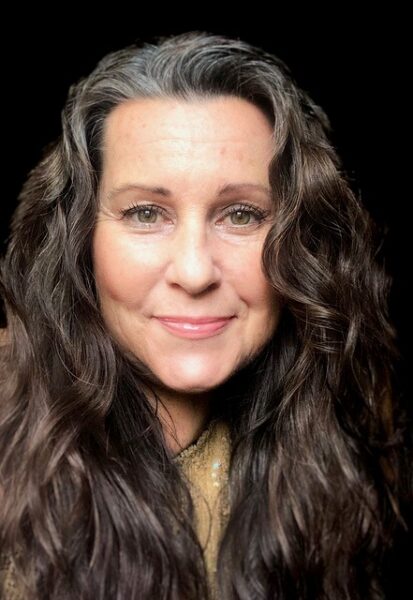 A headshot of Linda, who received better hearing from her cochlear implant, smiling with a black backdrop.