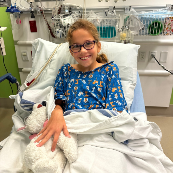 Savannah, whose hearing care team helped guide her to a cochlear implant. Pictured smiling in hospital bed, before her procedure.
