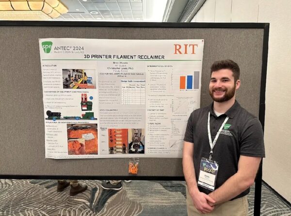 Broc, the 2025 Hear-o of the Year stands with a poster of his work at Rochester Institute of Technology.