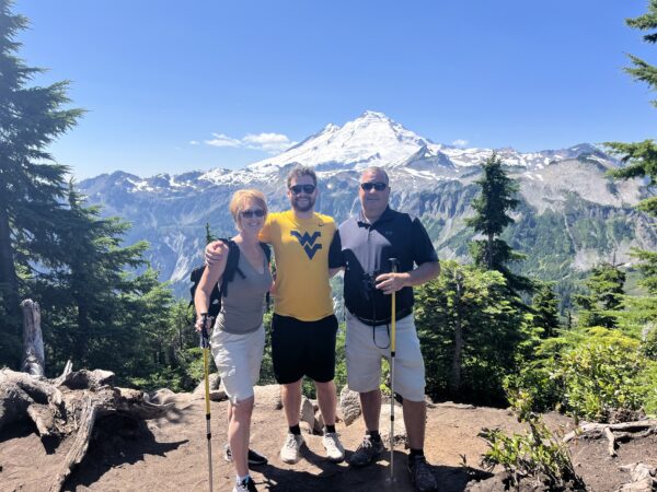 Broc, the 2025 Hear-o of the Year, stands between his mom and dad on a mountain hike with a mountain in the background.
