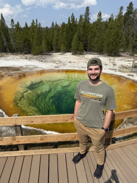 Broc, the 2025 Hear-o of the Year, stands in front of a geyser. 