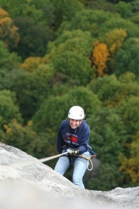 photo of a woman in a hard hat rappelling from rocks over the treeline; inspire us recipient artwork blog