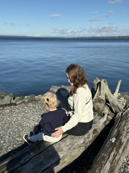 A picture over the shoulder of Lawson, and his mother Alisha, sitting on a log in front of a large body of water. Lawson's cochlear implant is visible on the back of his ear.