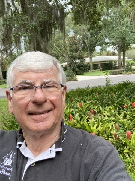 Gene, whose cochlear implant helped his career, taking a selfie in front of a large grouping of pink flowers. 